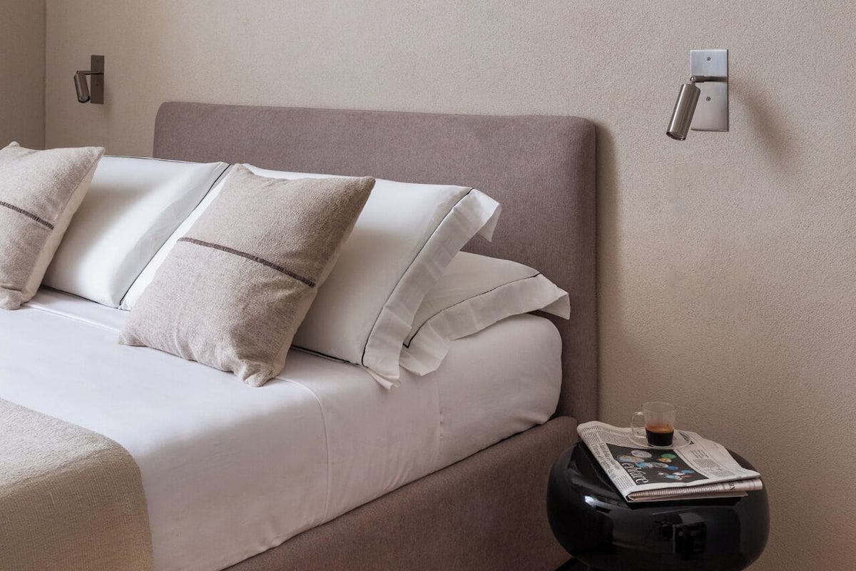 Une chambre à coucher avec un lit, des oreillers, une table de chevet et un luminaire fixé au mur.
