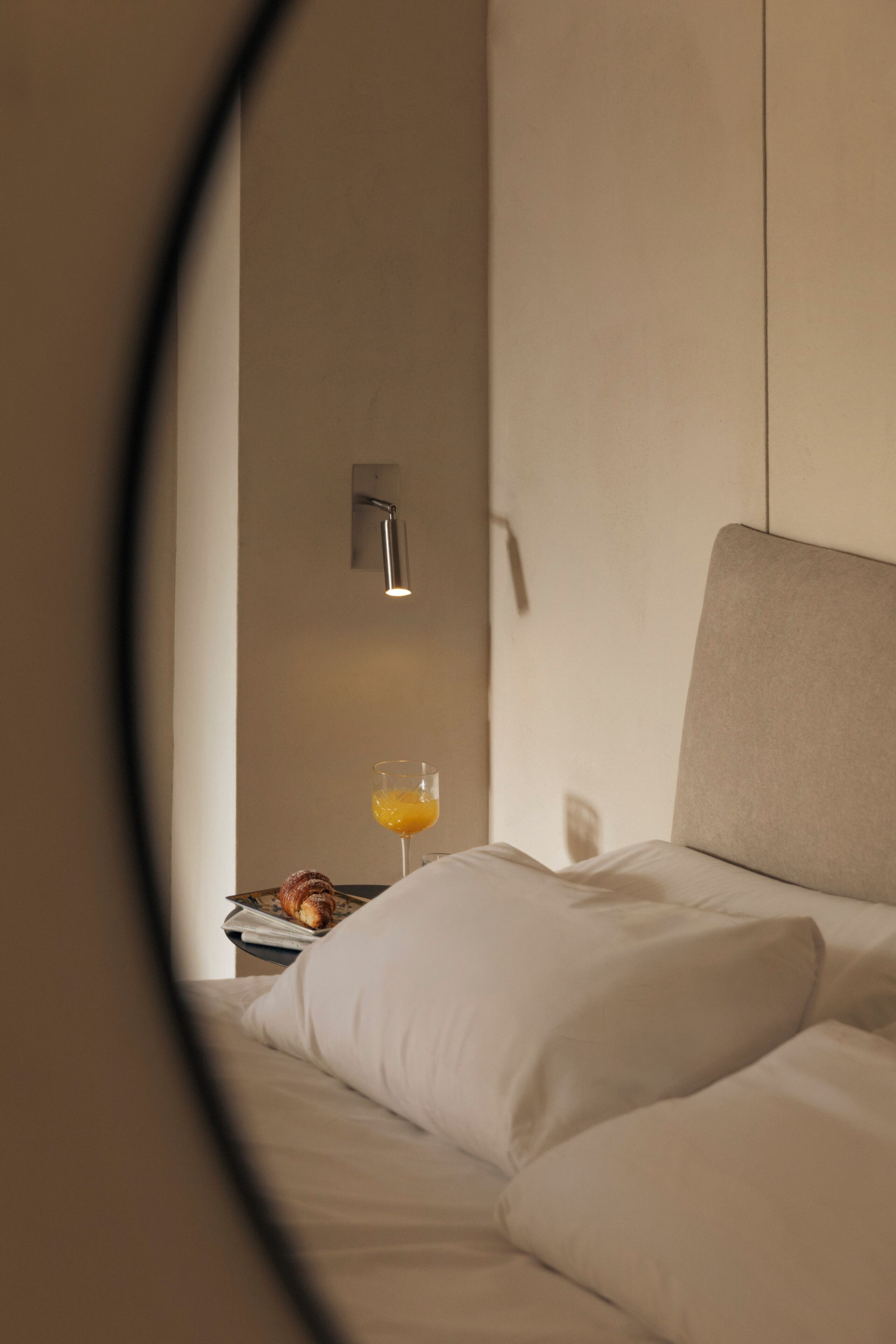 Ein Hotelzimmer mit einem Bett, einem Nachttisch mit Orangensaftgläser und einer Wandleuchte.