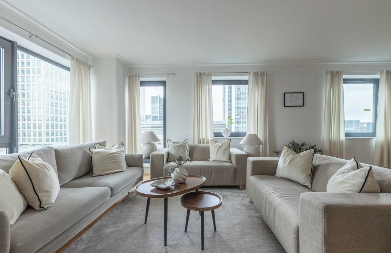 A modern living room with a sofa set, a coffee table, and a view of the cityscape through large windows.