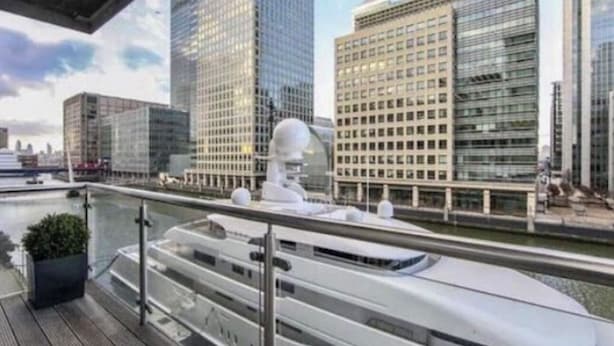 A modern yacht docked at a marina with a city skyline in the background. - High -Rise waterfront Apartment (London)