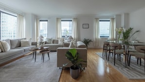 A modern living room with a sofa, coffee table, and dining area. - High -Rise waterfront Apartment (London)