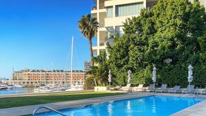 A swimming pool with a metal ladder, surrounded by lounge chairs and umbrellas, with a marina and buildings in the background. - The Marina V&A Waterfront by Smart City Stays (Cape Town)