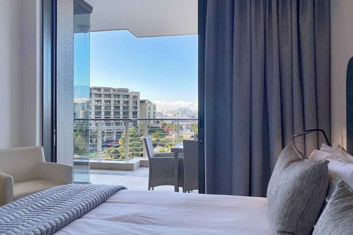 A hotel room with a bed, a chair, and a view of the cityscape through a large window.