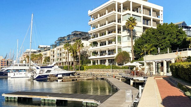 A waterfront hotel with multiple balconies, a marina with boats, and a pedestrian walkway. - The Marina V&A Waterfront by Smart City Stays (Cape Town)