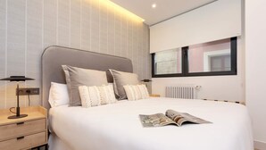 A modern bedroom with a large bed, a bedside table with a lamp, and a window with blinds. - Exclusive Apartment in Granada Center. Alhondiga II (Granada)