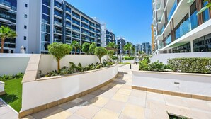 A modern building with multiple floors, balconies, and a landscaped area with trees and shrubs. - Luxury Studio in Azizi Riviera  (Dubai)