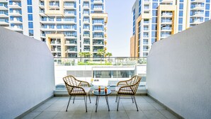 A balcony with two wicker chairs and a small round table, overlooking a modern residential building complex. - Luxury Studio in Azizi Riviera  (Dubai)