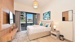 A modern hotel room with a large bed, a flat-screen TV, a wooden console, a balcony with a view, and a painting on the wall. - Luxury Studio in Azizi Riviera  (Dubai)