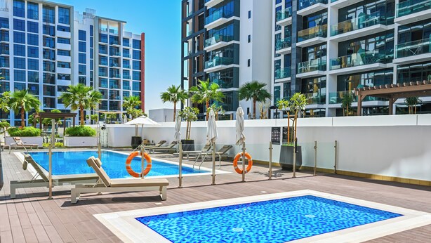 A rooftop swimming pool with lounge chairs and palm trees, surrounded by modern buildings. - Luxury Studio in Azizi Riviera  (Dubai)