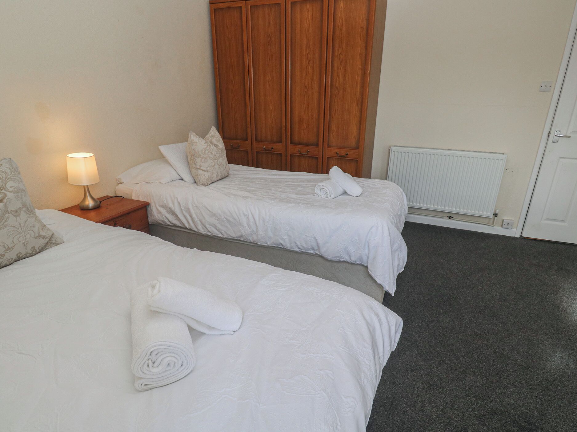 Een hotelkamer met twee bedden, een houten kledingkast, een nachtkastje met een lamp en een radiator.