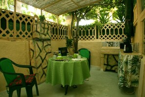 A covered outdoor dining area with a table set for two, surrounded by green chairs. - GREEN ROOM OF ARTISTS (Vada)