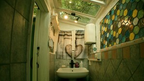 A bathroom with a white sink, a heart-shaped mirror, and a mosaic tile wall. - GREEN ROOM OF ARTISTS (Vada)