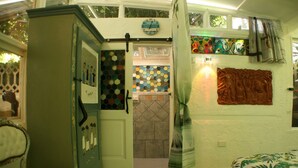 A room with a green wardrobe, a bed with a patterned bedspread, a wall clock, a colorful hexagonal tile backsplash, and a curtain. - GREEN ROOM OF ARTISTS (Vada)