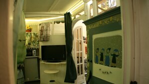 A compact room with a television, a small table, and a door with a decorative painting. - GREEN ROOM OF ARTISTS (Vada)