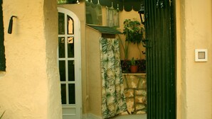 A narrow entrance with a white door, a green gate, and a small garden area with potted plants. - GREEN ROOM OF ARTISTS (Vada)