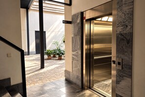 An elevator with a marble wall, a sign indicating the floor level, and a potted plant in the background. - Genteel Home Corral del Rey II (Seville)