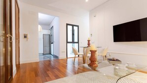 A modern living room with a glass coffee table, a flat-screen TV mounted on the wall, and a dining area with a table and chairs. - Modern Apartment in Seville. Corral del Rey II (Seville)