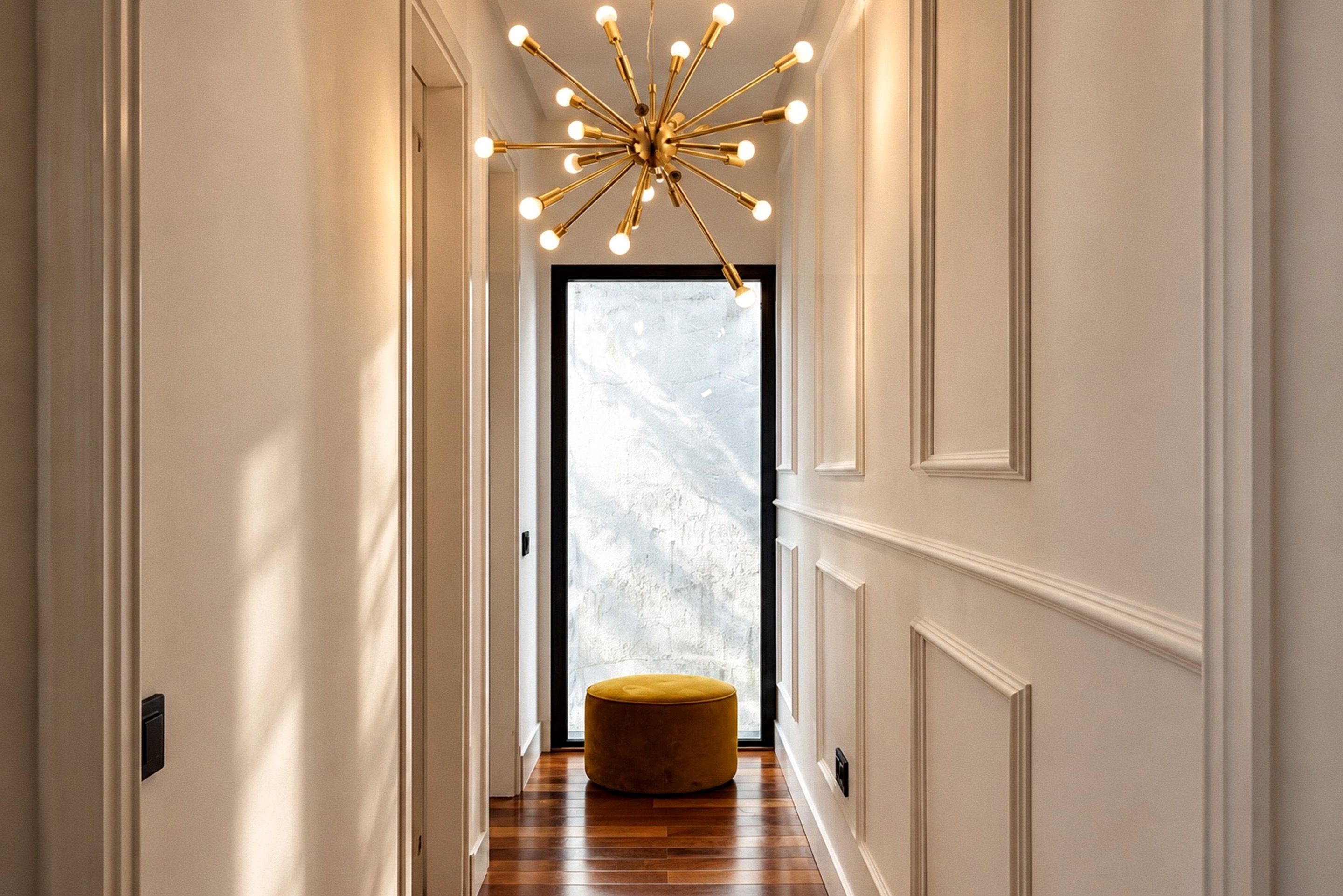 A hallway with a modern chandelier, a wooden floor, and a door with frosted glass.