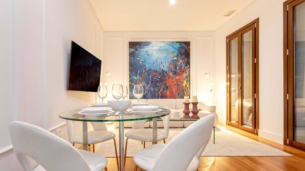 A dining area with a glass table, white chairs, and a large abstract painting on the wall. - Modern Apartment in Seville. Corral del Rey II (Seville)
