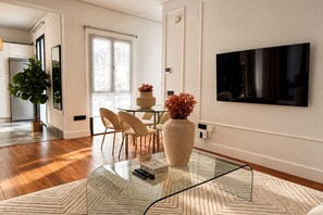 A modern living room with a glass coffee table, a flat-screen TV mounted on the wall, and a dining area with chairs and a table. - Genteel Home Corral del Rey II (Seville)