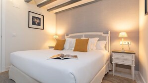 Ein ordentlich bezogenes Bett mit einer Zeitschrift, zwei Nachttischlampen und einem gerahmten Bild an der Wand.
