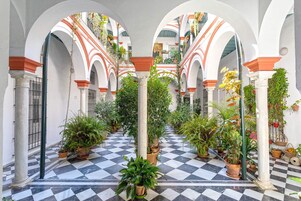 An indoor courtyard with a checkered floor, arches, columns, and potted plants.