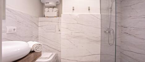 A modern bathroom with a marble floor, a glass-enclosed shower, a toilet, and a sink with a wooden countertop.