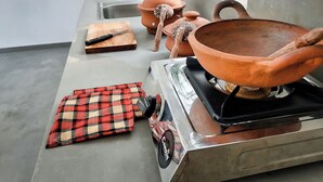 Een keuken met een gasfornuis, een snijplank, een mes, een rood-zwart geruit kleed en een grote terracotta pot.