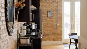 A kitchen with a brick wall, a mirror, a sink, a countertop, and a door leading to a balcony. - The Urban Alchemist Loft (Benton Harbor)