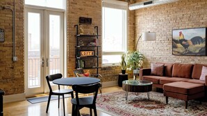 A living room with a brick wall, a sofa, a coffee table, a bookshelf, and a painting. - The Urban Alchemist Loft (Benton Harbor)
