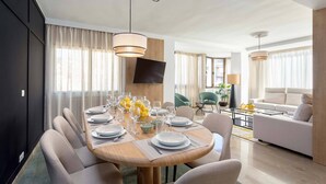 A modern dining area with a round wooden table set for six, surrounded by upholstered chairs. A flat-screen TV is mounted on the wall above the table. - Luxury Apartment in City Center. Puerta Real II (Granada)
