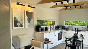 Une cuisine moderne avec des meubles blancs, un coin repas avec une table ronde et des chaises, et un coin salon confortable avec un canapé et une petite table d’appoint.
