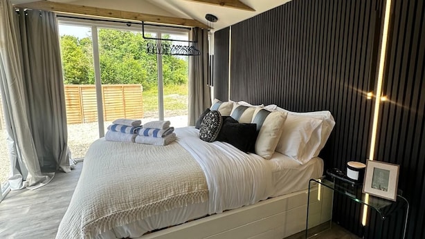 Une chambre à coucher moderne avec un grand lit, une table de chevet en verre et une vue sur l’extérieur.