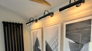 Un salon moderne avec un canapé, trois tableaux abstraits encadrés et un luminaire suspendu au plafond.