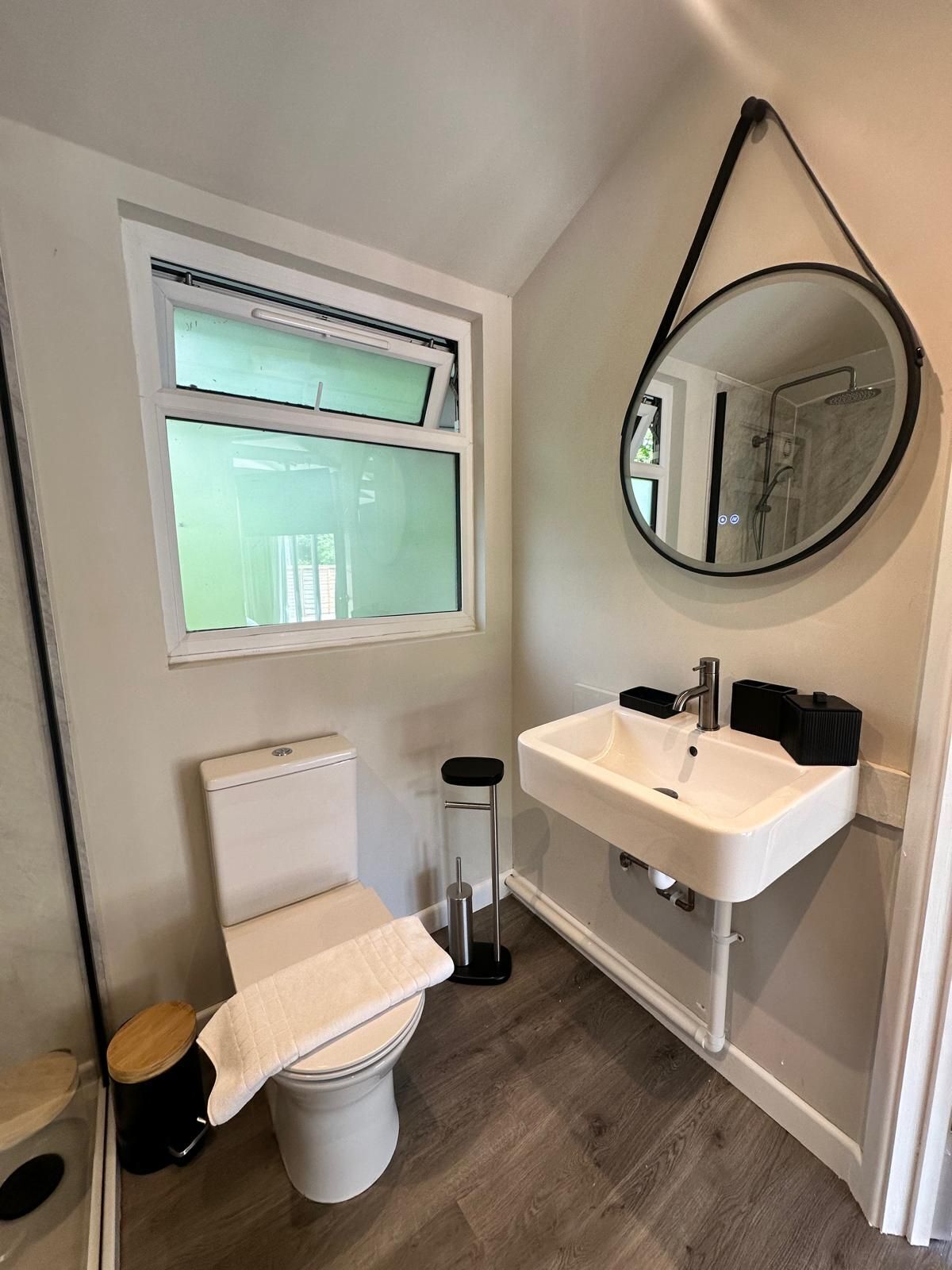 A compact bathroom with a toilet, a sink, a mirror, and a window.