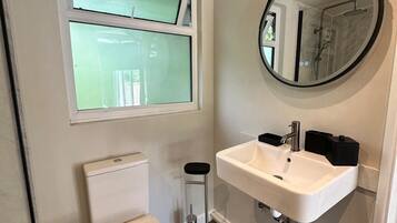 A compact bathroom with a toilet, a sink, a mirror, and a window.