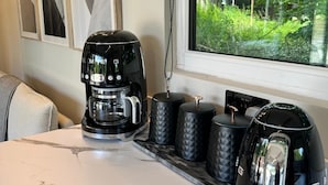 Une cuisine équipée d’une machine à café, de bouilloires et d’une fenêtre donnant sur un paysage verdoyant.