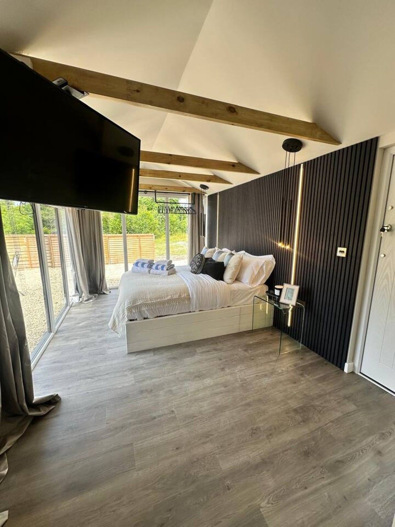 A bedroom with a bed, a TV mounted on the wall, and a view of the outdoors.