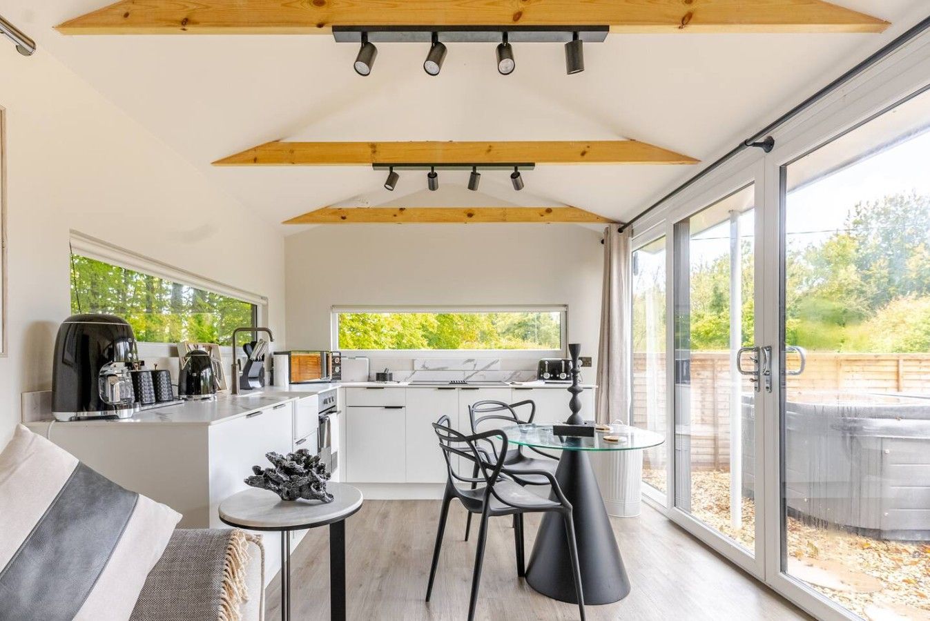 A modern kitchen with a dining area, large windows, and a view of greenery.