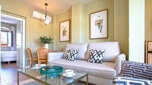 A living room with a sofa, coffee table, and chairs. There is a plant on a table and artwork on the wall.