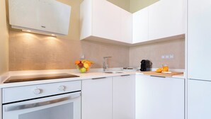 A modern kitchen with white cabinetry, a built-in oven, a sink, and a countertop with a fruit bowl and a coffee maker.