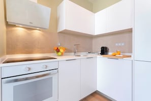 Cozinha moderna com armários brancos, forno embutido, pia e uma fruteira.