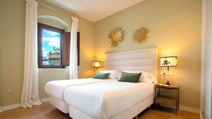 A double bed with white bedding, a bedside table with a lamp, and a window with curtains.