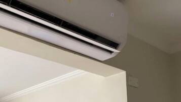 A room with a ceiling-mounted air conditioner, a framed picture on the wall, and a wooden cabinet.