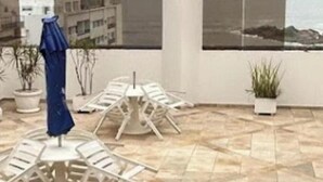 A rooftop terrace with a seating area, potted plants, and a view of the cityscape. - Flat Golden Beach Pitangueiras with Sea View (Guarujá)