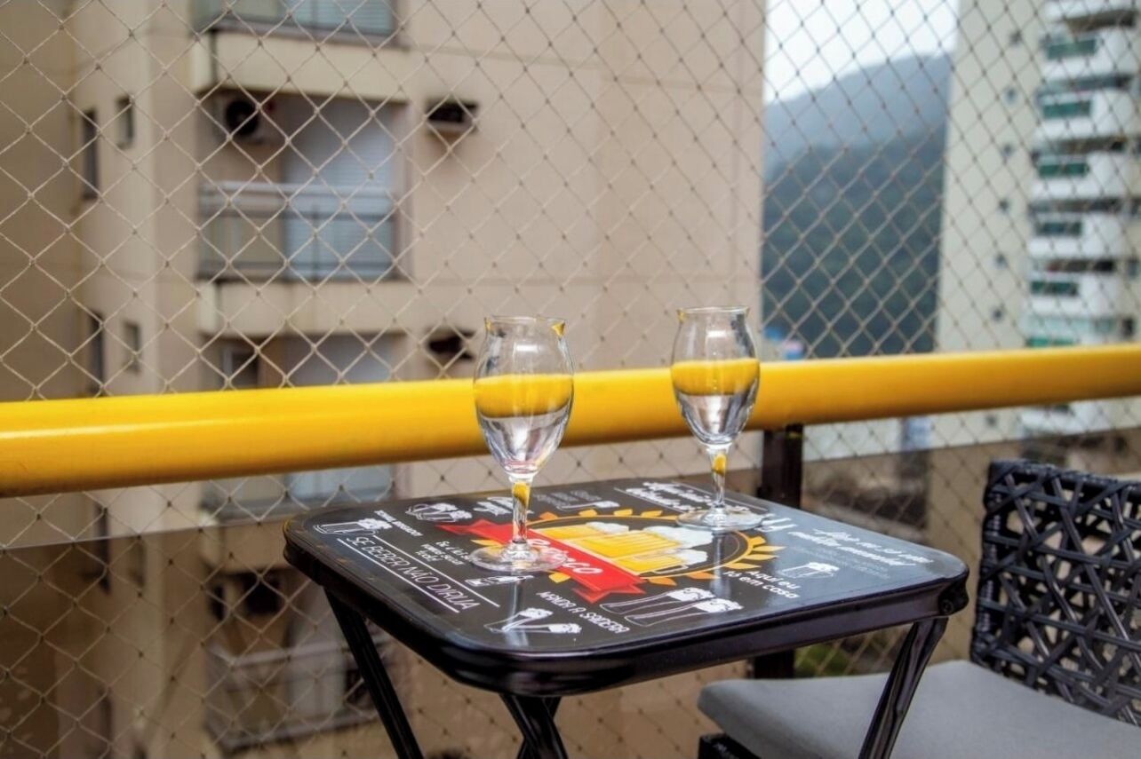 A table with two glasses of orange juice and a menu on a balcony with a yellow railing, overlooking a building.
