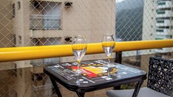 A table with two glasses of orange juice and a menu on a balcony with a yellow railing, overlooking a building.