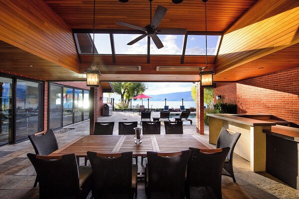 Un patio al aire libre con una mesa y sillas de madera, un ventilador de techo y vista al océano.