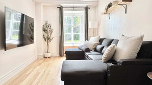 A modern living room with a dark grey sectional sofa, a flat-screen TV mounted on the wall, and a potted plant.