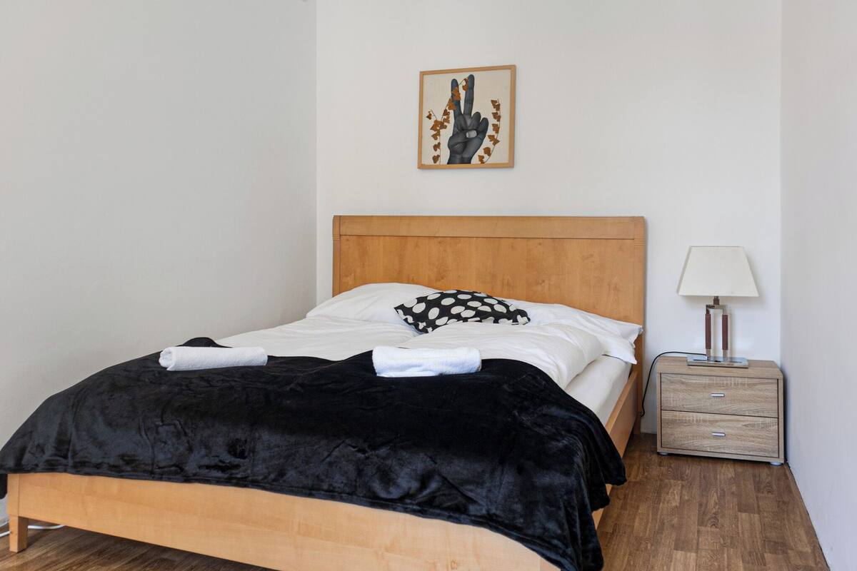 A neatly made bed with a black and white polka dot pillow, a wooden headboard, and a small bedside table with a lamp.